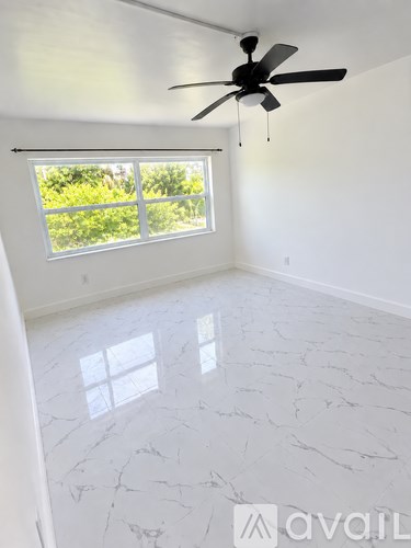 A room with a ceiling fan and a window overlooking greenery.