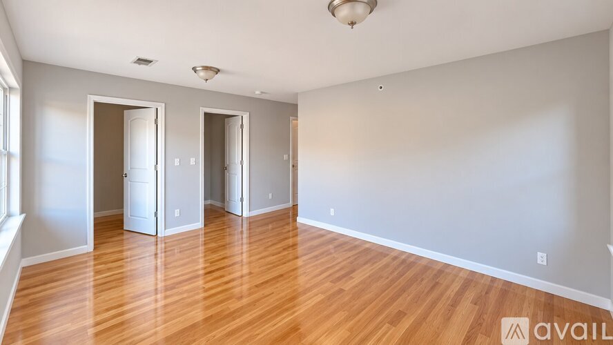 A room with wooden floors and white walls, with three doors and a window on the left.