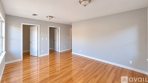 A room with wooden floors and white walls, with three doors and a window on the left.