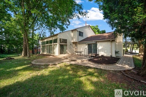 A house with a white exterior and a brown roof is surrounded by greenery.