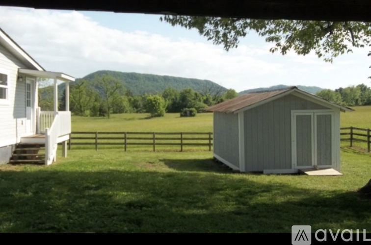 A small house with a porch and a shed in a grassy field.