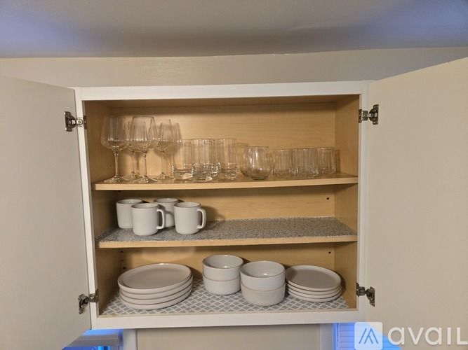 A kitchen cabinet with glasses, cups, and plates.