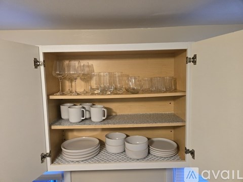 A kitchen cabinet with glasses, cups, and plates.