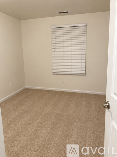 A room with beige carpet and a window with blinds.