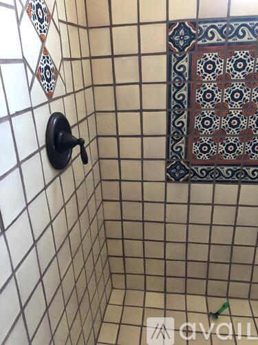 A shower with a black handle and a tile wall.