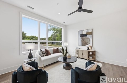 A living room with a black chair, a white couch, a table with a lamp and a plant on it, and a ceiling fan.