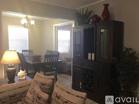 A living room with a black cabinet, a couch, a chair, a table with a lamp and a vase on it.