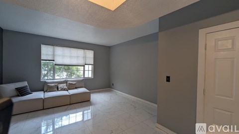 A living room with a white couch and a window with blinds.