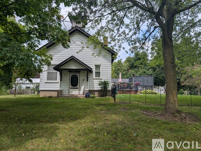 A small white house with a black roof and a tree in front.