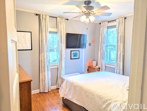 A bedroom with a bed, a ceiling fan, and a window with curtains.
