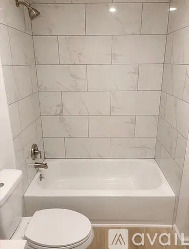 A white toilet sits next to a white bathtub in a bathroom with marble tile walls.