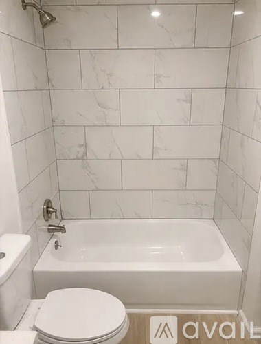 A white toilet sits next to a white bathtub in a bathroom with marble tile walls.