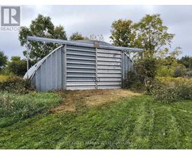 A large metal shed sits in a grassy field.