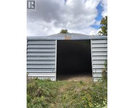 A large metal structure with a curved top and a doorway is surrounded by vegetation.
