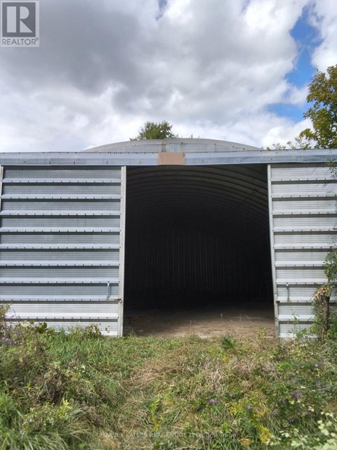A large metal structure with a curved top and a doorway is surrounded by vegetation.