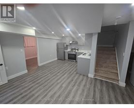 A room with a grey floor and white walls, with a kitchenette in the corner.