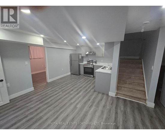A room with a grey floor and white walls, with a kitchenette in the corner.