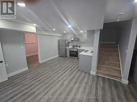 A room with a grey floor and white walls, with a kitchenette in the corner.