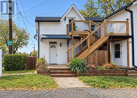 A white house with a wooden deck and stairs leading to the front door.