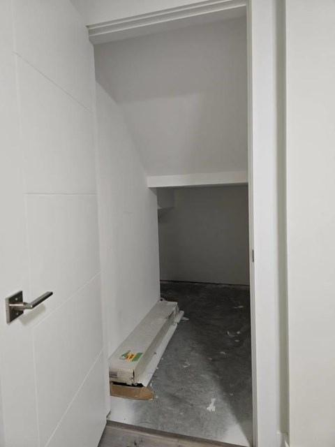 A white door with a silver handle is open to a room with a concrete floor and a white wall.