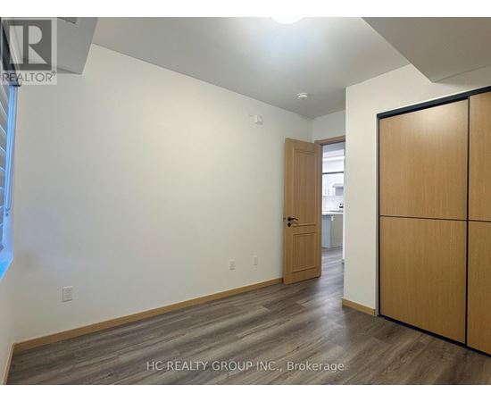 A room with a wooden floor and a slanted ceiling with a door on the right.