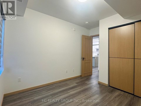 A room with a wooden floor and a slanted ceiling with a door on the right.