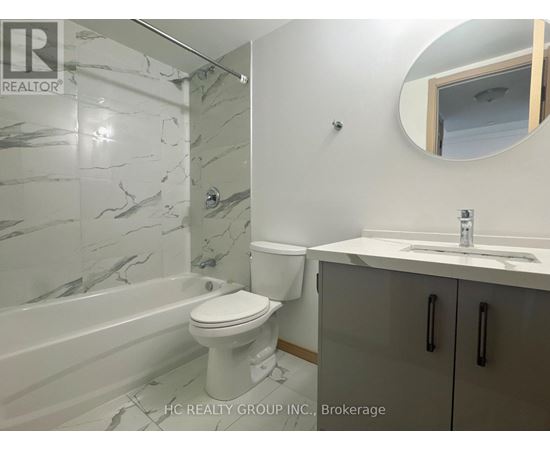 A bathroom with a marble tile shower, toilet, and sink.