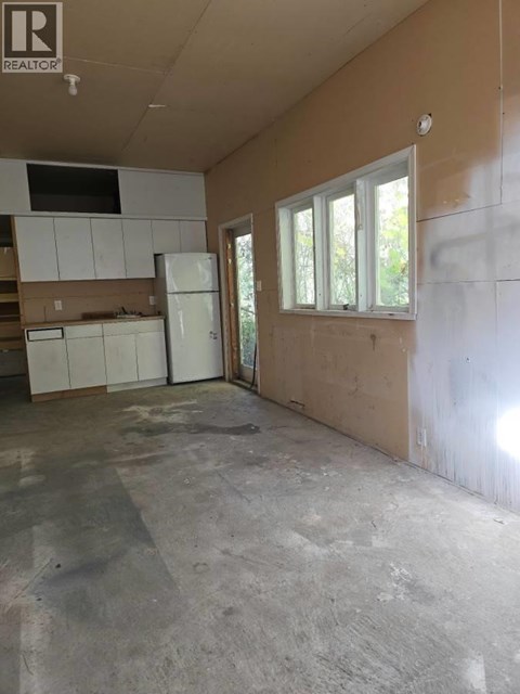 A room with a white fridge and cabinets in a house under construction.