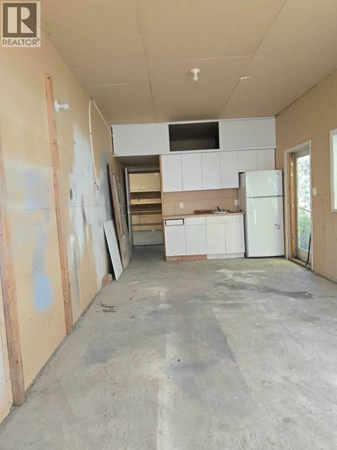 A room under construction with a white fridge and cabinets.