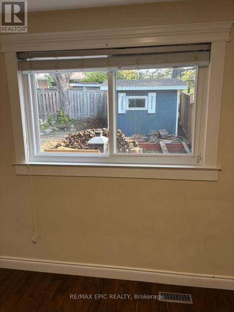 A window with a view of a blue shed and a wooden fence.