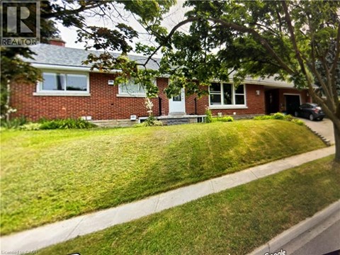 A house with a red brick exterior and a white door is surrounded by a green lawn.