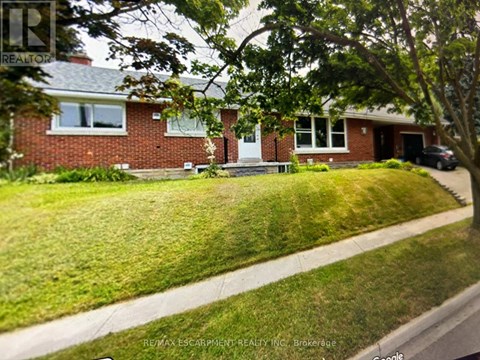 A house with a red brick exterior and a white door is surrounded by a green lawn.