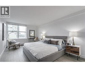 A bedroom with a large bed, a chair, and a nightstand with a lamp.