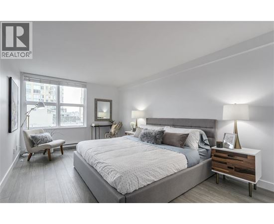 A bedroom with a large bed, a chair, and a nightstand with a lamp.