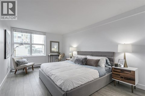 A bedroom with a large bed, a chair, and a nightstand with a lamp.