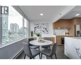 A modern dining room with a table set for two and a city view through the window.