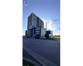 A tall building with a glass facade stands next to a street with cars parked on the side.
