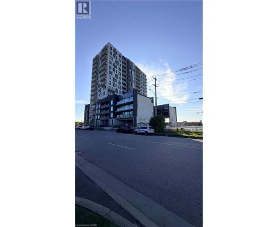 A tall building with a glass facade stands next to a street with cars parked on the side.