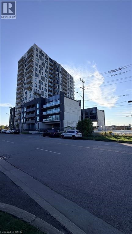 A tall building with a glass facade stands next to a street with cars parked on the side.
