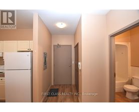 A hallway with a toilet and a sink visible through the door.