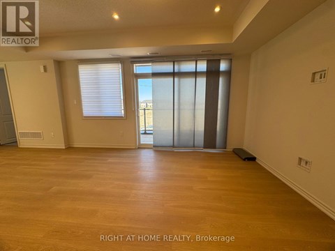 A spacious room with wooden flooring and a sliding glass door.