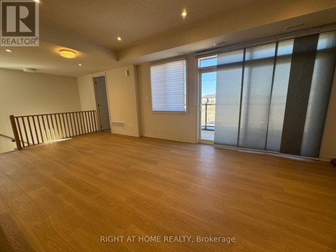 A spacious room with wooden flooring and large windows.