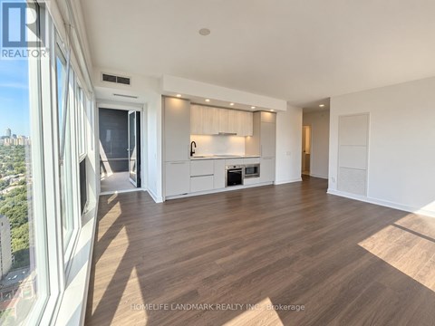 A spacious living room with wooden flooring and a large window overlooking the city.