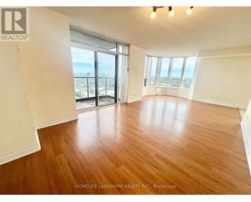 A spacious room with wooden flooring and large windows overlooking a cityscape.