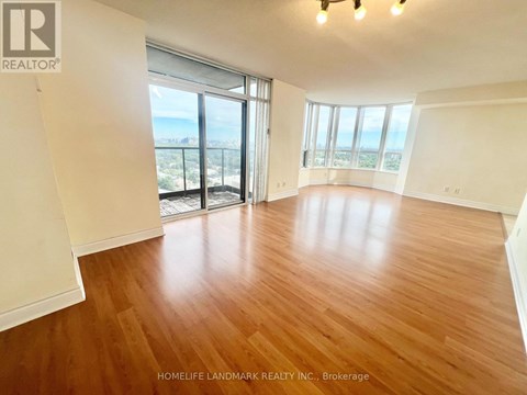 A spacious room with wooden flooring and large windows overlooking a cityscape.