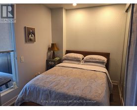 A bedroom with a bed, nightstand, lamp, and a picture of a dog on the wall.
