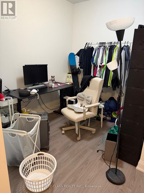 A room with a desk, chair, and clothes hanging on a rack.
