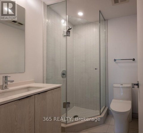 A bathroom with a glass shower stall and a toilet.
