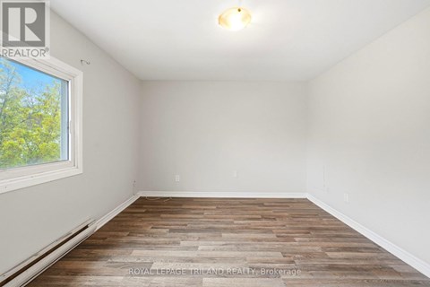 A room with wooden flooring and a window showing trees outside.