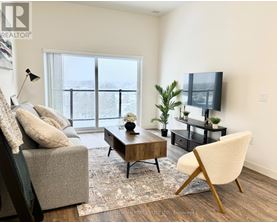 A living room with a grey couch, a wooden coffee table, a white chair, and a flat screen TV.